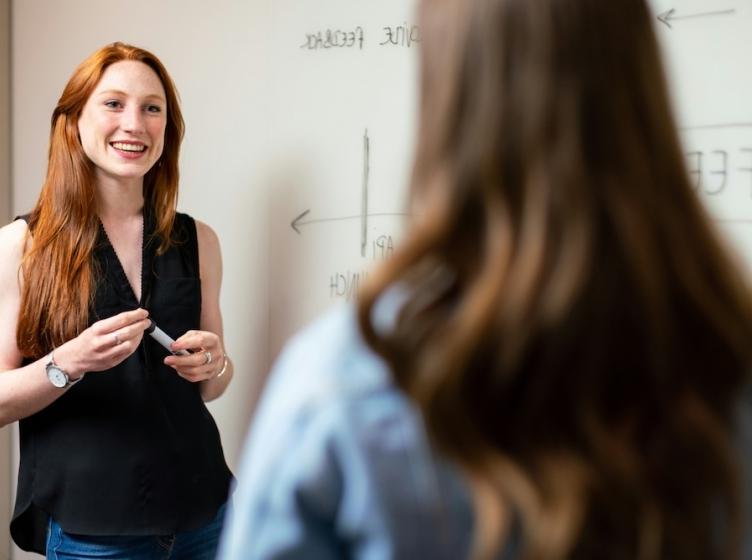 Female teacher standing in front of a whiteboard while talking with a student